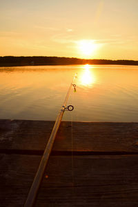 Fishing rod on pier over lake against sky during sunset