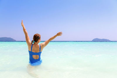 Rear view of woman with arms raised standing in sea against sky