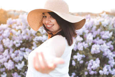 Side view of woman wearing hat standing against flowers