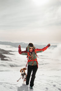 Rear view of woman with dog on snow covered field against sky during sunset