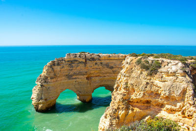 Rock formations in sea against clear blue sky