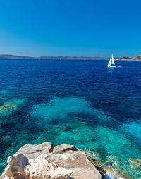 Sailboat sailing in sea against clear blue sky
