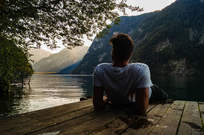 Rear view of man sitting on lake against mountain