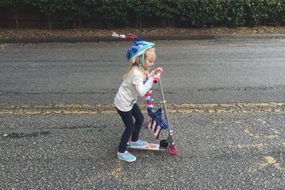 Side view of girl riding push cart on road