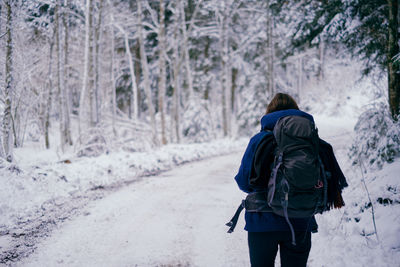 Rear view of woman with backpack walking in snow covered forest