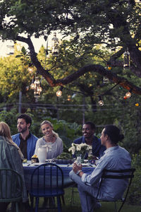 Happy multi-ethnic friends sitting at outdoor food table during evening party