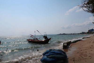 Fishing boat on sea shore against sky