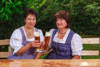 Mature female friends holding beer glasses while sitting at park