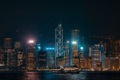 Illuminated buildings by river against sky at night