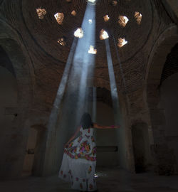 Rear view of woman standing by sunlight streaming through ceiling holes