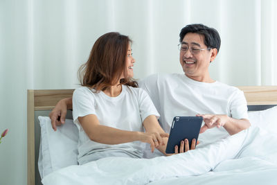 Man and woman using phone while sitting on bed