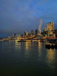 Illuminated buildings by river against sky at night