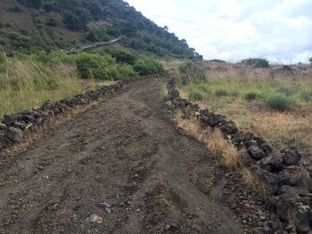 Dirt road amidst land against sky