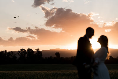 Rear view of woman standing on field against sky during sunset