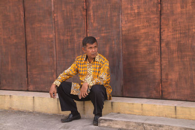 Full length of man sitting against wall