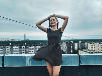 Portrait of smiling young woman standing on roof against sky