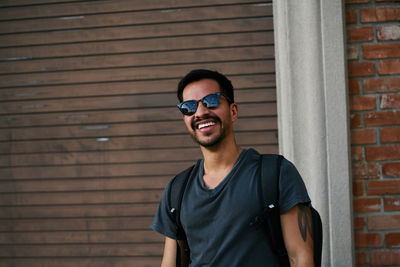 Portrait of young man wearing sunglasses standing against brick wall