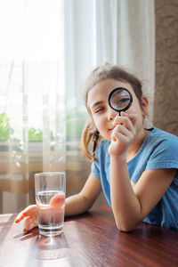 Portrait of girl looking through magnifying glass at home