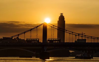 Silhouette chelsea bridge over thames river against sunset sky