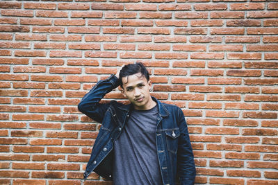 Portrait of young man standing against brick wall