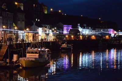 Sailboats moored in illuminated city by sea at night