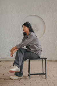 Young woman using mobile phone while sitting against wall