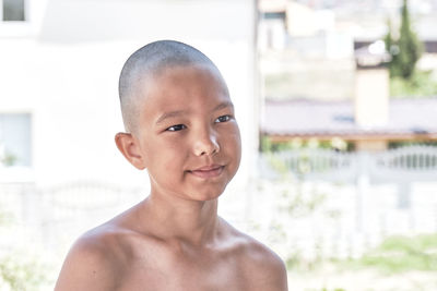 Summer shoulder portrait of a tanned asian boy with a bald haircut.