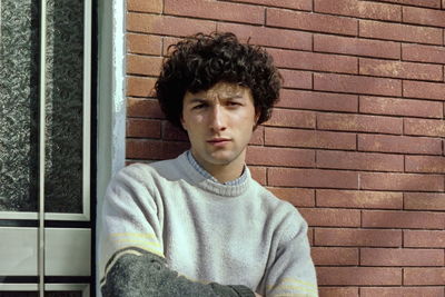 Portrait of young man sitting against wall