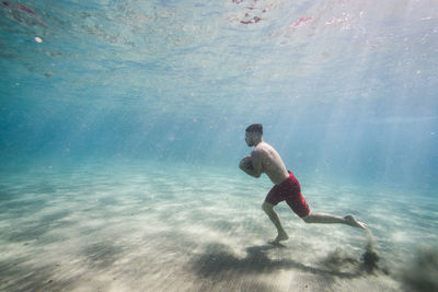 Full length of shirtless man with rock running underwater