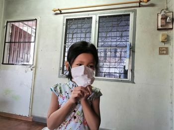 Girl wearing mask looking away while standing at home