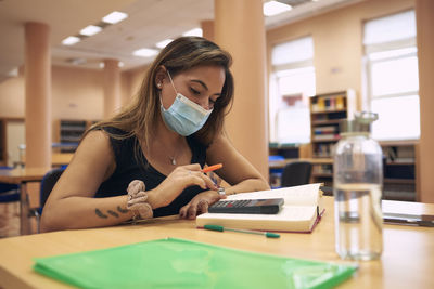 A young woman with a surgical mask studying in the university library