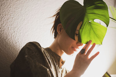 Asian woman peaks through plant leaf in lamp light at home