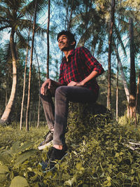 Low angle view of young man sitting on tree stump in forest