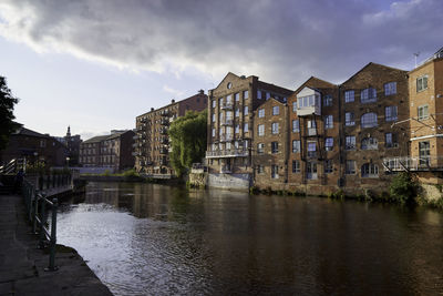 Bridge over river by buildings in city against sky