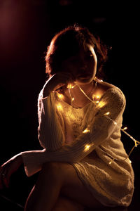Young woman with illuminated string lights sitting against black background