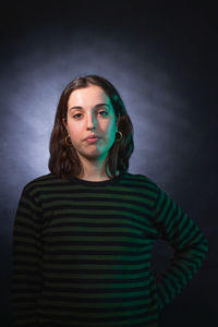 Portrait of young woman standing against black background
