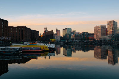 Reflection of boats and buildings on river against sky during sunset