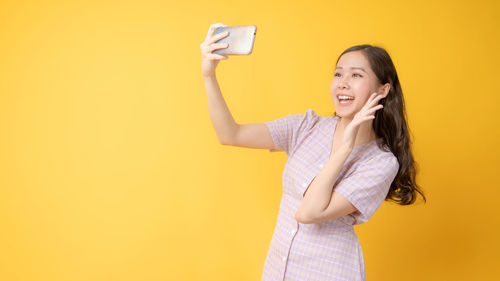 Smiling young woman using mobile phone against yellow background