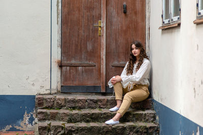 Portrait of woman sitting on steps against closed door