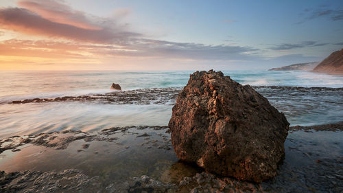 Rock at beach against sky during sunset