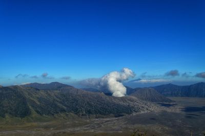 Smoke emitting from volcanic mountain against blue sky