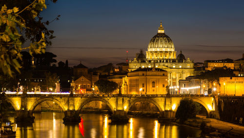 Illuminated arch bridge over river against buildings in city