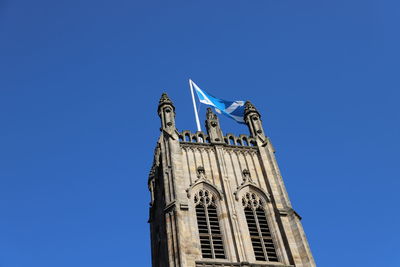 Closeup image of church tower with saltire flag flying in blue sky