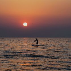 Silhouette man in sea against sunset sky