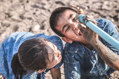 High angle view of siblings drinking water from faucet