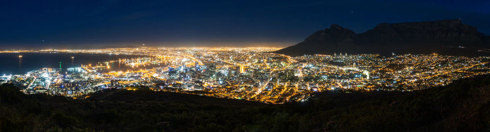 High angle view of illuminated city by sea against sky at night