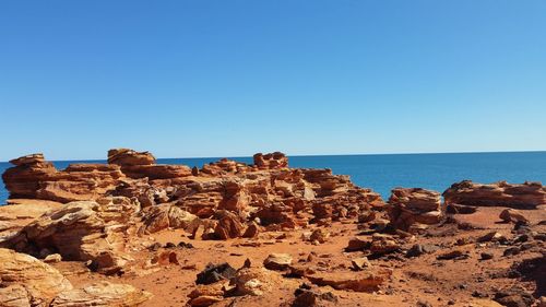 Rock formation by sea against clear blue sky