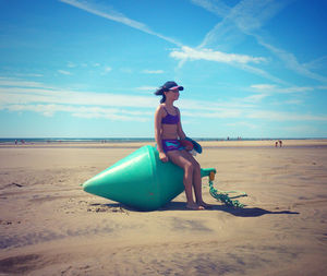 Smiling girl sitting on buoy at beach against sky