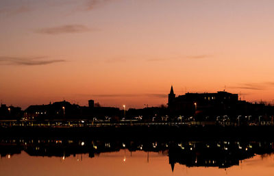 Silhouette buildings by sea against romantic sky at sunset