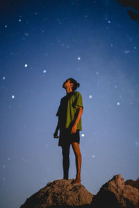 Low angle view of man standing on rock against blue sky